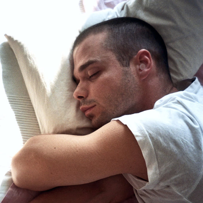 Man sleeping with Loop Dream peach earplugs in ears