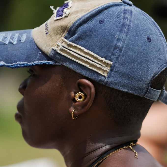 Person wearing a blue and beige cap with a blurred background wearing Loop Switch 2 earplugs in gold